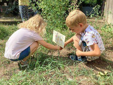 Zwei Kinder untersuchen ein kleines Schild im Gras.