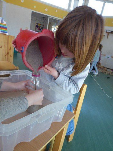 Kind schüttet Sand in eine Flasche.